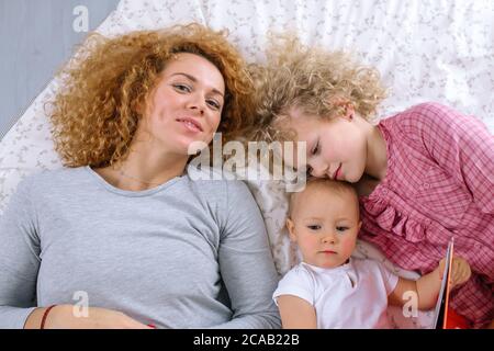 Draufsicht auf schöne junge Mutter und ihre Töchter Blick auf Kamera und lächelnd, während auf dem Bett liegen. Familie, Kindheit Konzept Stockfoto