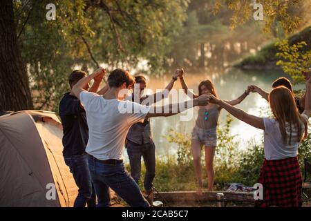 Freundliche Jugendliche machen Kreis und Spaß auf dem Campingplatz. Freizeit. Rest-Konzept. Wunderbare See und Wald auf dem Hintergrund des Fotos Stockfoto