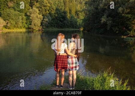 Zwei beste Freunde umarmen und schauen sich gegenseitig an, während sie am Ufer des Flusses stehen. Rückansicht Foto. Freundschaftskonzept Stockfoto