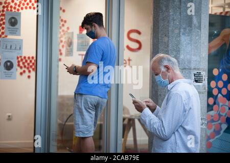 BELGRAD, SERBIEN - 28. JULI 2020: Alter älterer Mann mit einer Atemschutzmask, der sein Handy und seine Apps benutzt, während ein junger Mann das gleiche mit einer sma macht Stockfoto