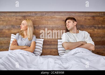 Junge kaukasische Mann versuchen, seine Freundin zu beruhigen, Situation zu lösen und mit ihr zu sprechen, sie auf dem Bett liegen von ihm abwenden, beleidigte Frau Stockfoto