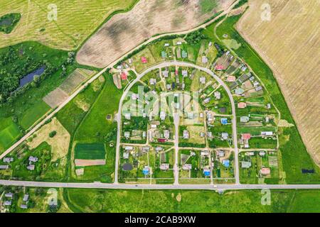 Top down Luftdrohne Bild von Dorf in der Landschaft zwischen grünen landwirtschaftlichen Feldern Stockfoto