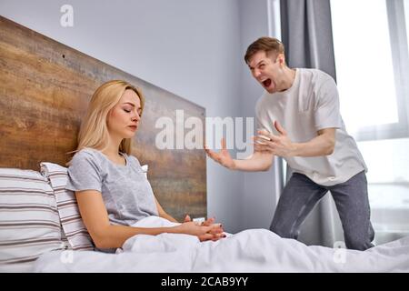 Hysterische Ehemann drückt Unzufriedenheit aus, Frau kümmert sich nicht, sitzen auf dem Bett ohne Emotionen, sie ist emotional verwüstet Stockfoto