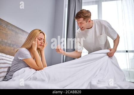 Wie viel kann man sitzen beleidigt, tun die Hausarbeit unzufrieden Mann wollen ihre faule Frau Hausarbeit zu tun, beleidigte Frau sitzt auf dem Bett Stockfoto