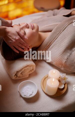 Schöne Frau im Bademantel bekommen Gesichtsmassage von weiblichen Händen im Spa-Salon Stockfoto