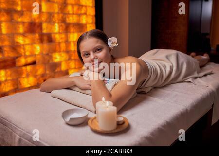 Porträt einer schönen lächelnden Frau, die nach oder vor dem Spa-Eingriff auf dem Tisch liegt, sich auf dem Rücken massiert, die Kamera anschaut und sich entspannt. Spa, Gesundheitswesen, Stockfoto