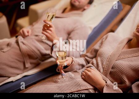 Junge kaukasische Paar kümmern sich um Körper zusammen im Spa-Salon liegen und trinken Champagner, trägt Bademantel Stockfoto