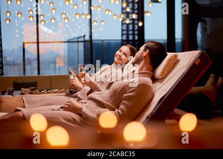 Junge kaukasische Paar kümmern sich um Körper zusammen im Spa-Salon liegen und trinken Champagner, trägt Bademantel Stockfoto