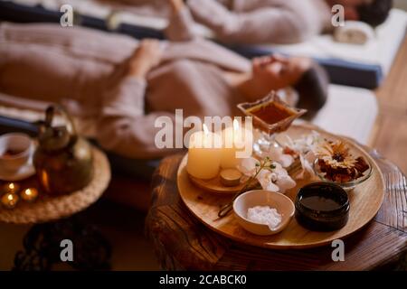 Kaukasische Männer und Frauen bei Spa-Behandlungen Entspannen und trinken Tee, während sie sich in speziellen Betten im Spa-Salon, Bademäntel tragen, um Kerzen Stockfoto