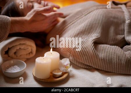 Junge Mädchen mit Massage auf ihr Gesicht im Spa Salon. Tragen Bademantel, Kerzen in der Nähe von ihr. Schönheitsbehandlung Stockfoto