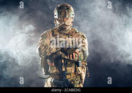 Junger Militärangehörige blickt selbstbewusst in rauchigen Räumen auf die Kamera, trägt grüne Uniform für Soldaten und Helm Stockfoto