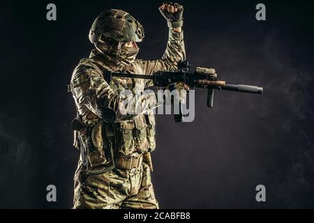 Junge Soldaten der russischen Streitkräfte stehen in rauchigen nebligen Raum mit Gewehr, tragen grüne Uniform, Helm und mit Sonderausrüstung Stockfoto