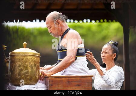 Eine alte Frau trägt einen Gürtel zu einem balinesischen hinduistischen Zeremonienmeister Stockfoto