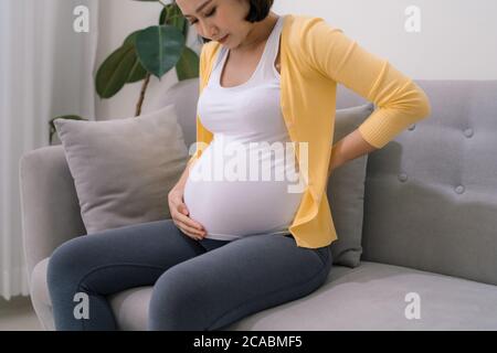Junge schwangere Frau mit Rückenschmerzen zu Hause Stockfoto