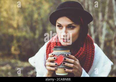 Junge Frau in einem schwarzen Hut trinkt Kaffee aus gemütlichen Tasse auf die Natur. Braun getöntes Foto Stockfoto