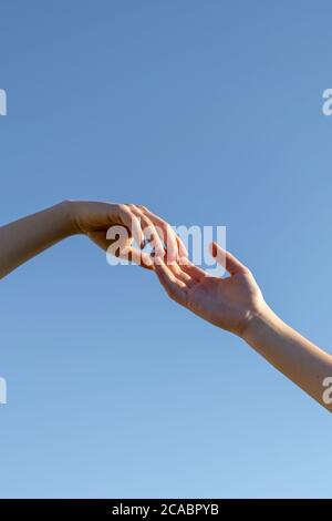 Vertikale Aufnahme von zwei Händen, die sich gegenseitig ausstreten Auf einem blauen Himmel Hintergrund Stockfoto