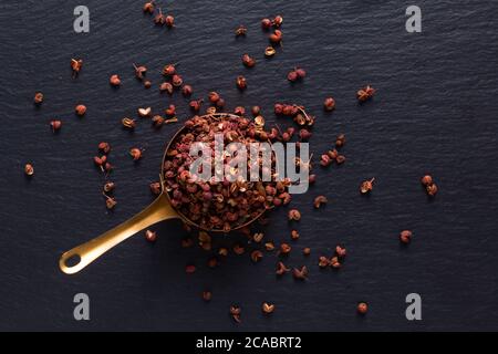 Food Gewürzen Konzept Draufsicht auf Bio Sichuan, Szechuan Pfeffer in Kupferbecher auf schwarzem Schiefer Stein mit Kopierraum Stockfoto