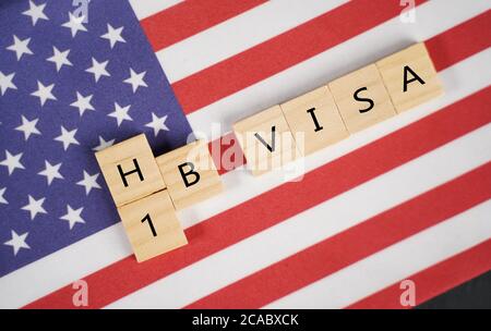 Konzept des H1B Visa für ausländische Arbeitnehmer mit Holzbuchstaben mit US-Flagge oder US-Flagge als Hintergrund Stockfoto