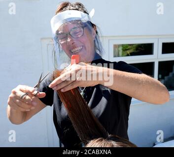 Fröhliche Swansea Friseur Rosalba Gambatesa wendet ihre Fähigkeiten im Freien und trägt ein Gesichtsvisier zum Schutz. Stockfoto