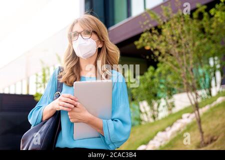 Nahaufnahme einer Geschäftsfrau mittleren Alters, die Gesichtsmaske auf der Straße trägt, während sie zur Arbeit geht. Stockfoto