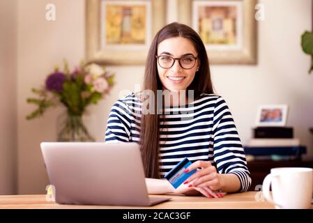 Schöne junge Frau hält ihre Kreditkarte und macht Online-Banking auf Laptop. Stockfoto