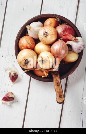 Zwiebeln und Knoblauch in einer Schüssel auf weißem Holzhintergrund, Draufsicht. Stockfoto