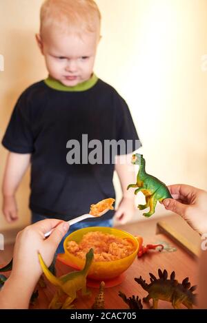 Mama füttert Spielzeug Dinosaurier aus einem Löffel, Mama spielt mit ihrem Sohn. Stockfoto