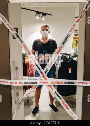 Budva, Montenegro - 01. august 2020: Ein Mann mit einer medizinischen Maske nimmt ein Selfie im Spiegel einer Garderobe in einem NewYorker Bekleidungsgeschäft, bedeckt Stockfoto