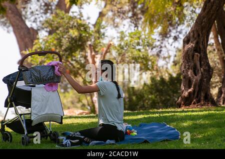 Freizeit unter COVID-19 Einschränkungen Menschen in einem Park mit Schutzmasken sitzen in einem Abstand zwischen den Gruppen und Einzelpersonen. Der Ausbruch von COVID Stockfoto