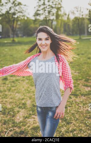 Schöne Hipster Mädchen in roten karierten Hemd, graues T-Shirt und zerrissene blaue Jeans in einem lässigen Stil tanzen und lächeln in grüner Natur Stockfoto