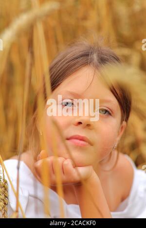 Kleines Mädchen mit einem Blumenstrauß in den Händen in einem Weizenfeld. Stockfoto