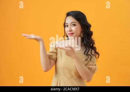 Beauty Frau mit charmanten Lächeln und zeigen Sie etwas zu Ihnen auf gelbem Hintergrund, asiatische Schönheit Stockfoto