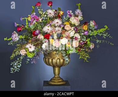 Ein schöner großer Blumenstrauß mit vielen verschiedenen Blumen in einem goldenen Topf, auf blauem Hintergrund Stockfoto