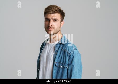 Porträt eines brutalen unrasierten Mannes, der auf grauem Hintergrund isoliert posiert und die Kamera anschaut Stockfoto