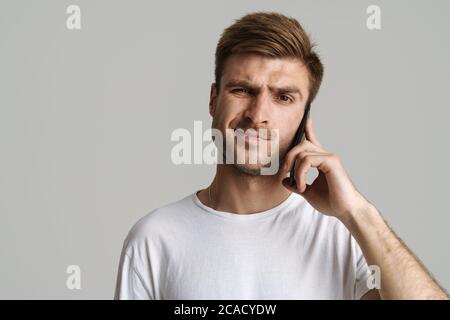 Porträt von schönen unzufrieden Mann sprechen auf Handy isoliert auf grauem Hintergrund Stockfoto