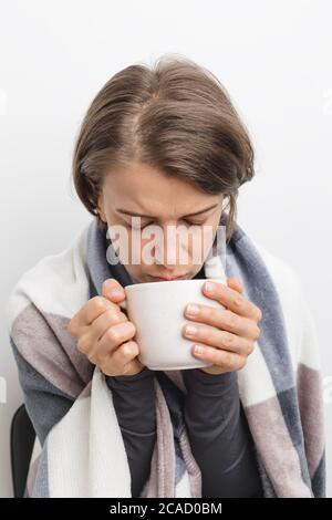 Eine kranke, kalte Frau trinkt Tee in einer Decke. Stockfoto