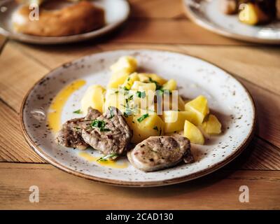 BEAF Scheiben und gekochte Kartoffeln. Authentischer Schuss Teller mit gebratenem Brot oder Schweinefleisch und Kartoffeln auf rustikalem Holztisch. Stockfoto