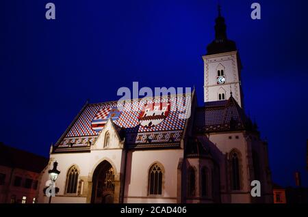 Markuskirche in Zagreb, Kroatien, beleuchtet und im Kontrast zum dunkelblauen und bewölkten Abend im Hintergrund. Stockfoto