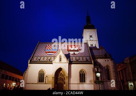 Markuskirche in Zagreb, Kroatien, beleuchtet und im Kontrast zum dunkelblauen und bewölkten Abend im Hintergrund. Stockfoto