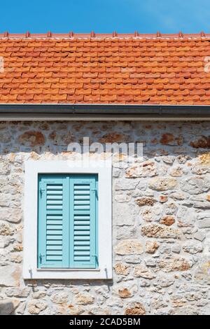 Geschlossenes Fenster mit türkisfarbenen Jalousien auf einem alten mediterranen Haus mit Steinmauer. Architektur, Reisen, Tourismus und Urlaubskonzepte. Stockfoto