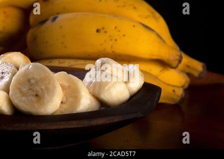 Ein Bündel Bananen und eine in Scheiben geschnittene Banane in einer Schüssel auf einem Tisch Stockfoto