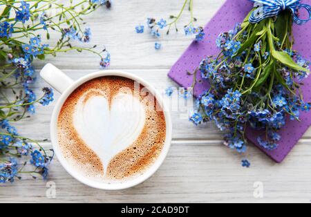 Blaue Vergissmeinnicht-Blumen, Notizbuch und eine Tasse heißen Kaffee. Das Konzept der Feiertage und Guten Morgen Wünsche. Stockfoto