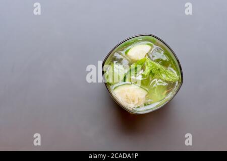 Blick von oben auf ein Glas Mojito Cocktail. Eiswürfel, Minzblätter und Zitronenscheibe innen. Grauer Tischhintergrund Stockfoto