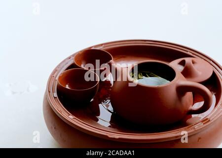Nahaufnahme rot braun Keramik Ton gefeuert Teekanne und Teetassen auf weißem Hintergrund. Frische Teeblätter schwimmen auf Teeswasser. Traditionelle chinesische Teekultur Stockfoto