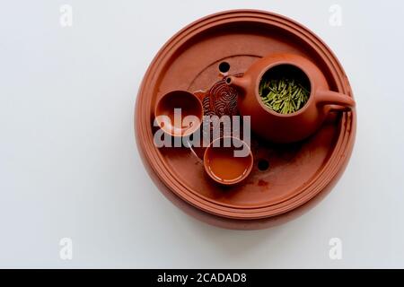 Draufsicht auf rot braun Keramik Sand gefeuerten Teekanne und Teetassen auf weißem Hintergrund. Frische Teeblätter schwimmen auf Teeswasser. Stockfoto