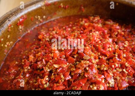 Nahaufnahme frisch gehackter Chilischote in braunem Keramikglas unter natürlichem Tageslicht. Beliebte chinesische Gerichte und Gewürze. Weichfokus Stockfoto