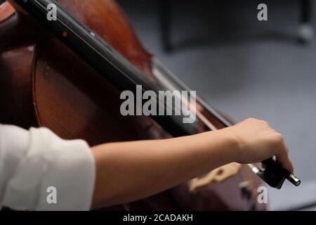 Nahaufnahme des Armes einer Musikerin, die sich verbeugt und braunes Cello spielt. Hintergrund verwischen Stockfoto