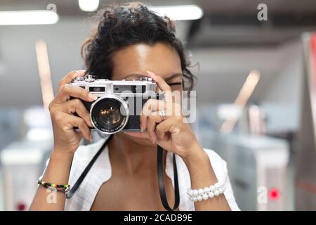 Nahaufnahme einer Frau mit exotischen Funktionen, die mit einer analogen Filmkamera fotografiert. Selektiver Fokus. Konzept von Reisen und Tourismus. Stockfoto