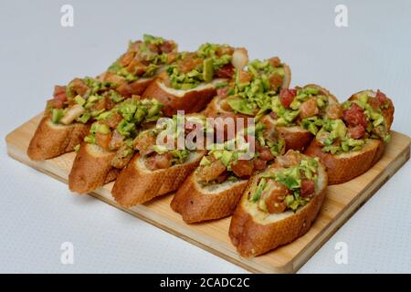 Schließen Sie viele Tapas auf Holzbrett. Spanisches Essen. Lachsfisch und Avocado-Salat auf geröstetem Brot. Verwischen Sie weißen Hintergrund Stockfoto