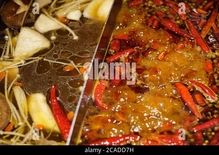 Nahaufnahme des traditionellen chinesischen Kochtopfes mit doppeltem Geschmack. Rote Paprika und Gemüse auf kochender Suppe. Hintergrund verwischen Stockfoto